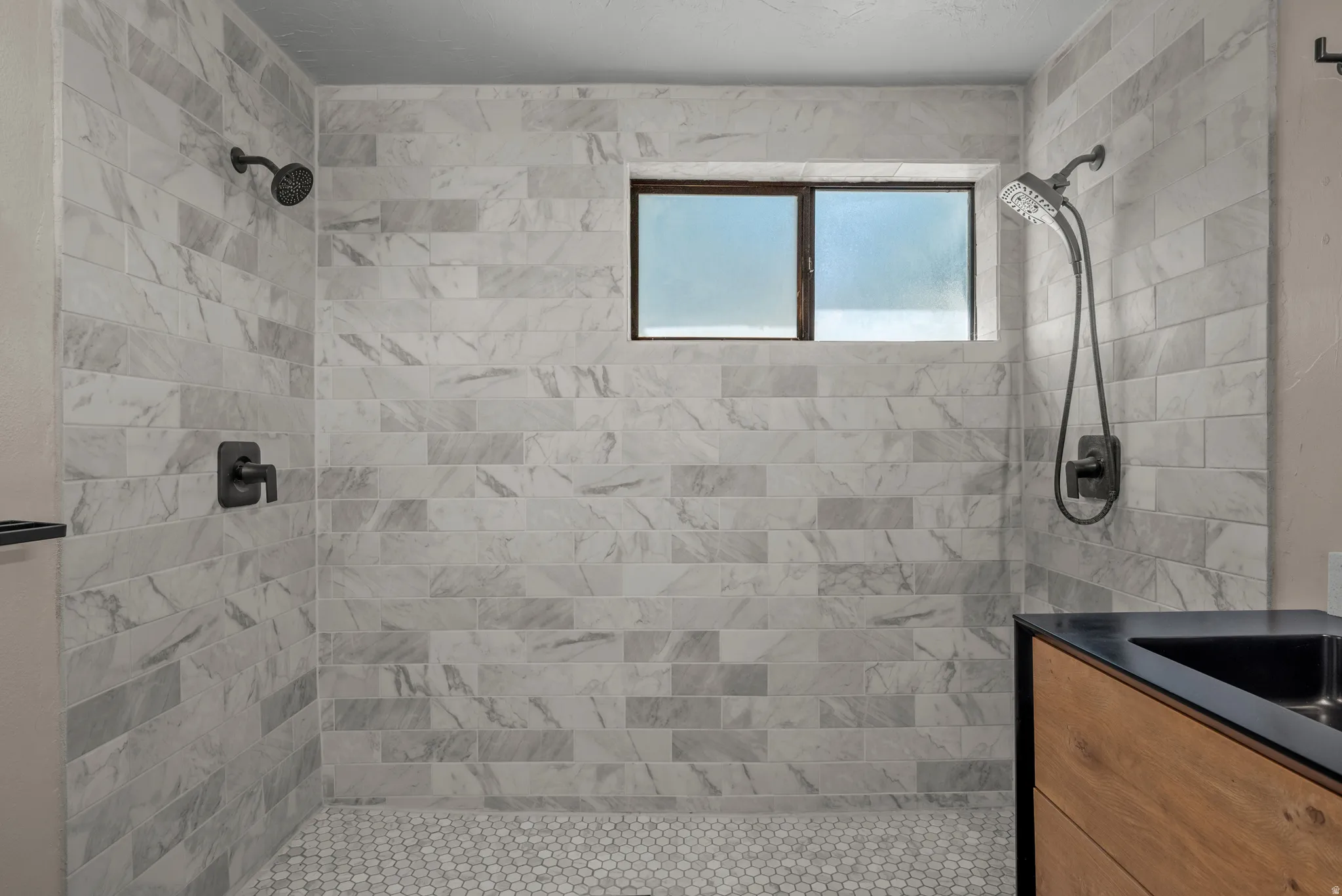 Shower stall with marble-look subway tile walls and hexagonal floor tile
