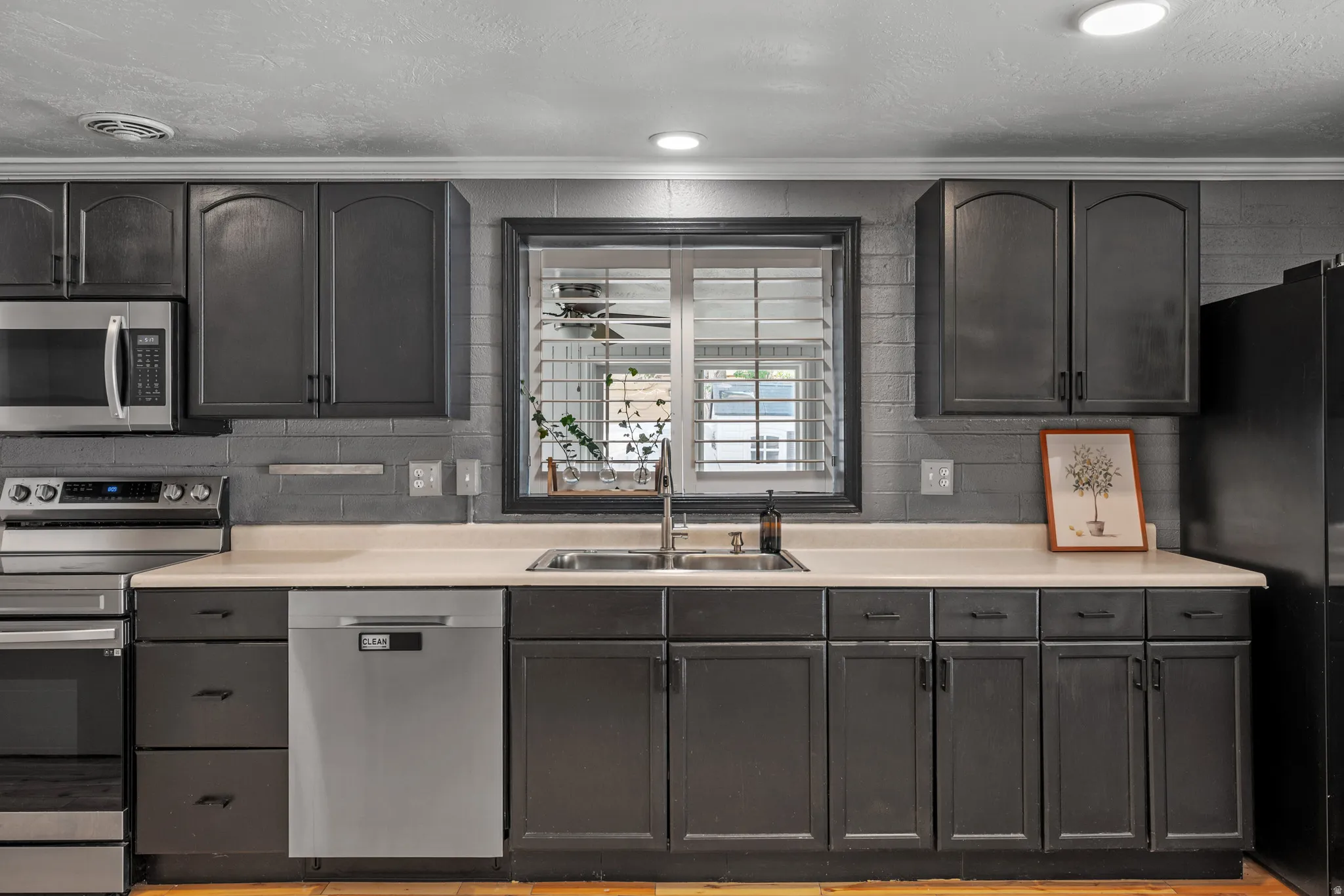 Gray cabinetry with dark hardware, undermount double-basin sink, light-toned countertops, tile backsplash, and stainless steel dishwasher