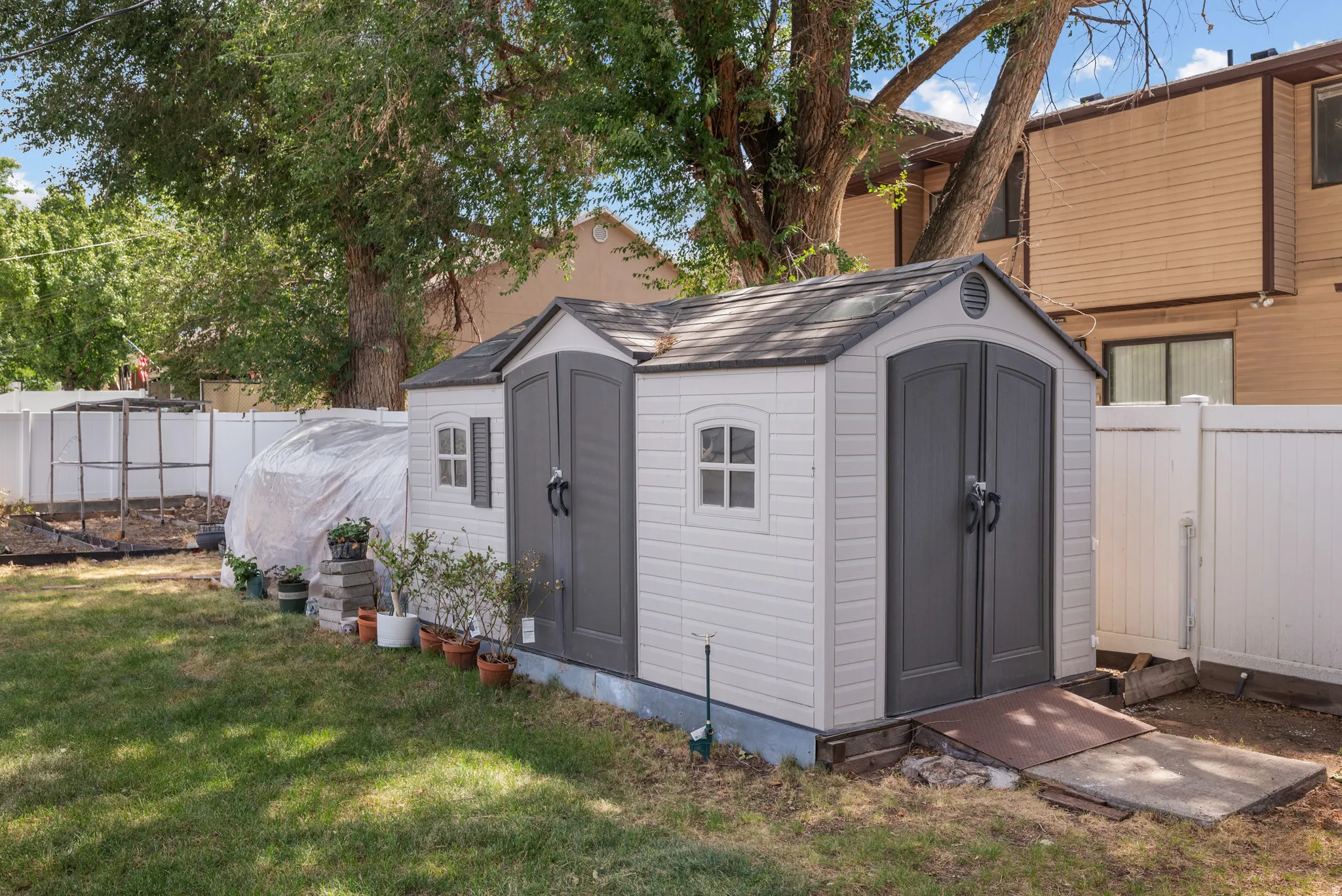 Backyard featuring a shed with double doors, white privacy fencing, and mature trees