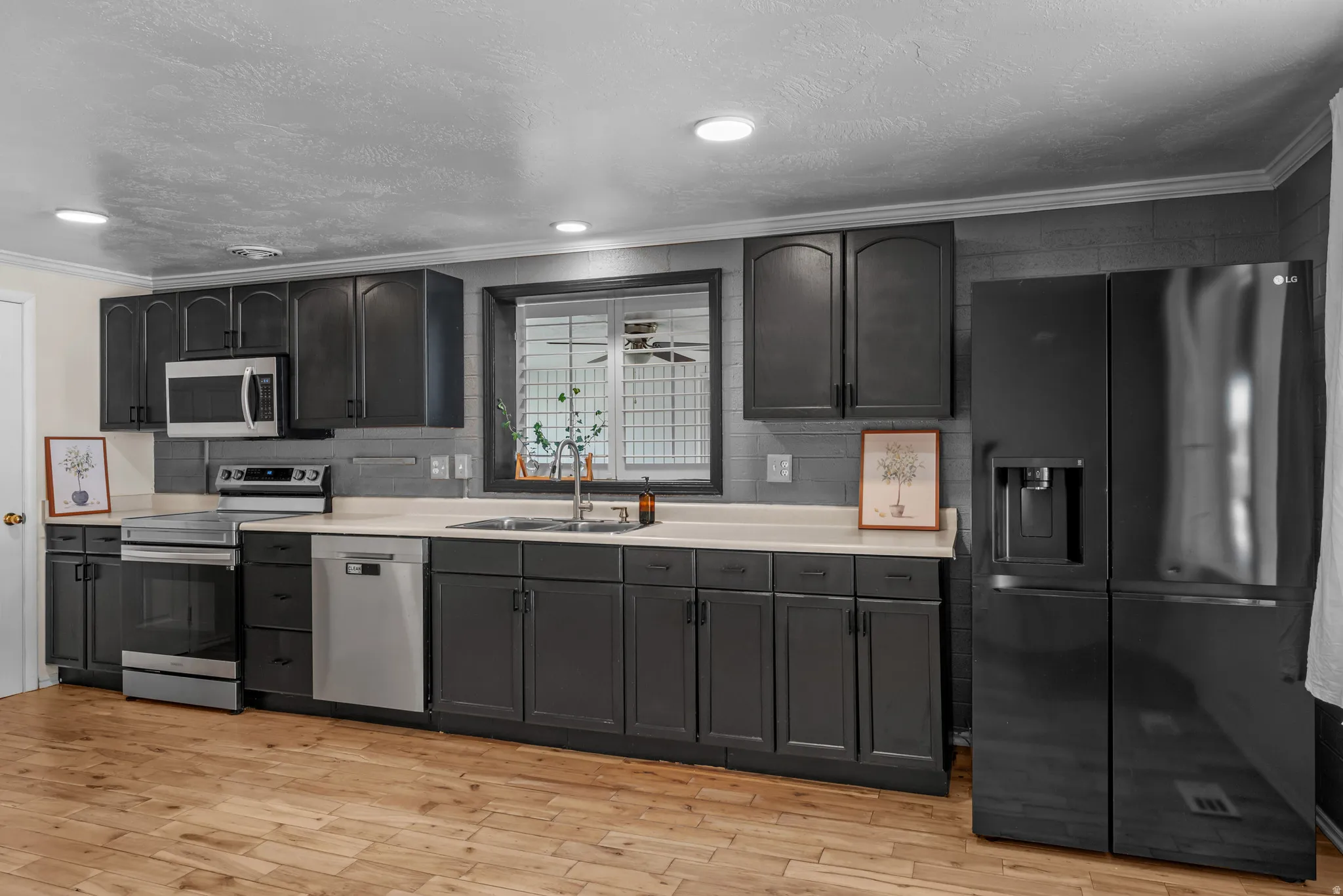 Kitchen featuring dark cabinetry, stainless steel appliances, a tile backsplash, light-toned countertops, and wood-finish flooring
