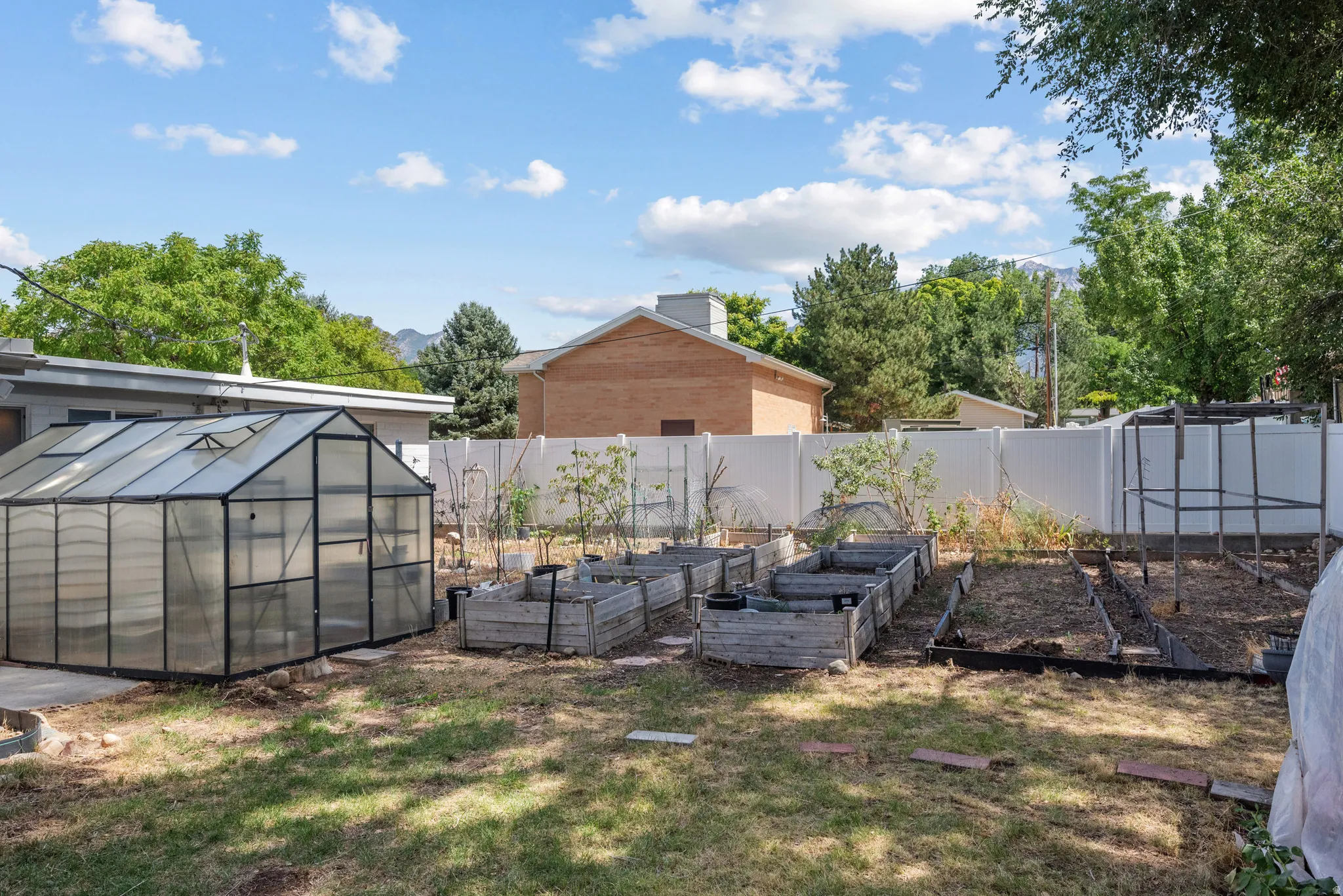 Backyard featuring a greenhouse, multiple raised garden beds, and a white privacy fence