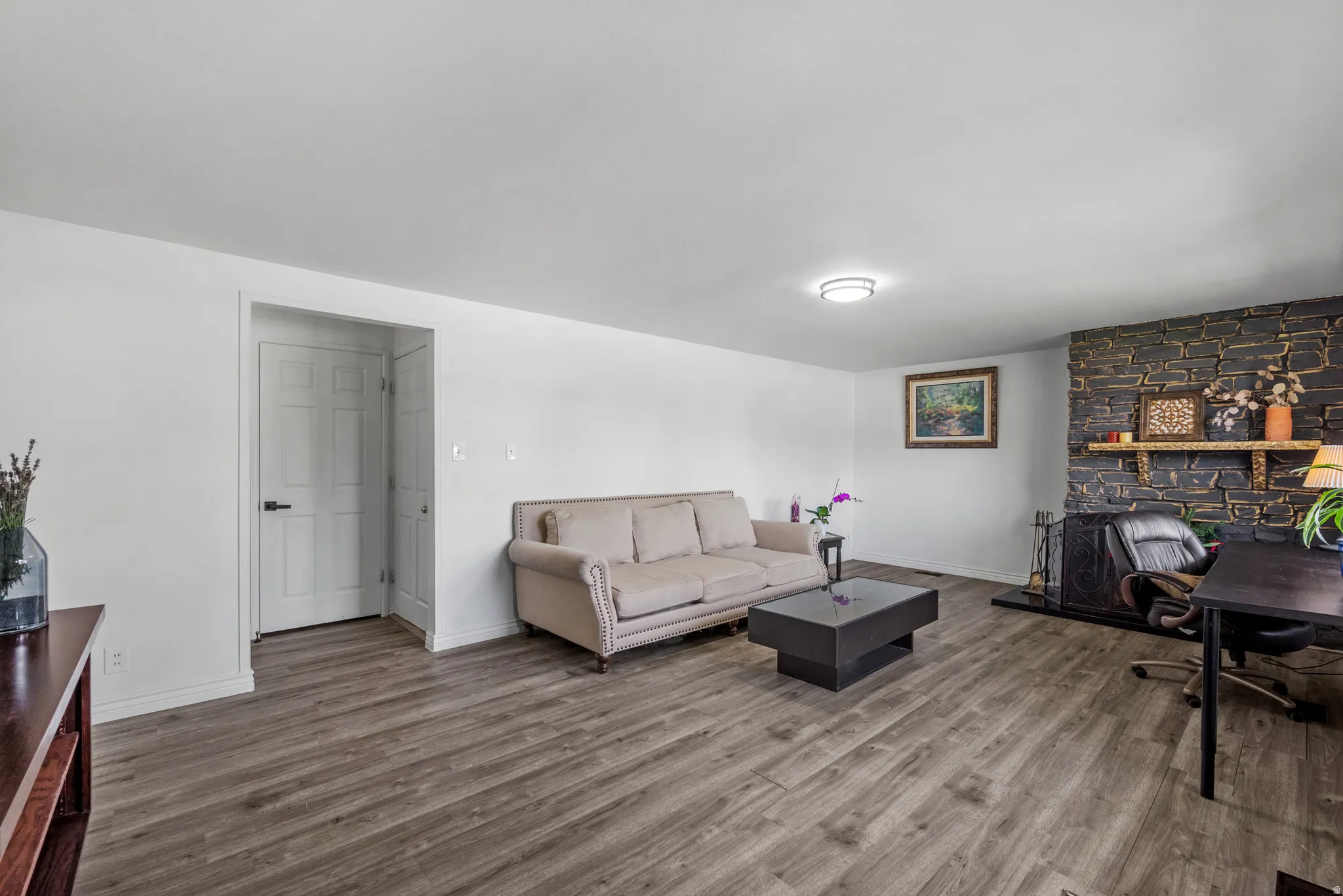 Spacious living area featuring wood-finish flooring, a white paneled door, and a stone-clad fireplace with a natural wood mantel