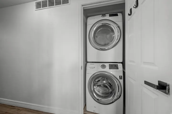 Stackable front-load washer and dryer set in a dedicated utility closet, featuring a white paneled door with a contemporary black lever handle and wall-mounted hooks