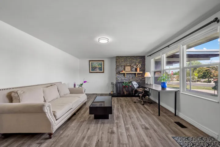 Wood-finish flooring, stone-clad fireplace with wood mantle, large multi-pane windows, and a flush-mount ceiling light