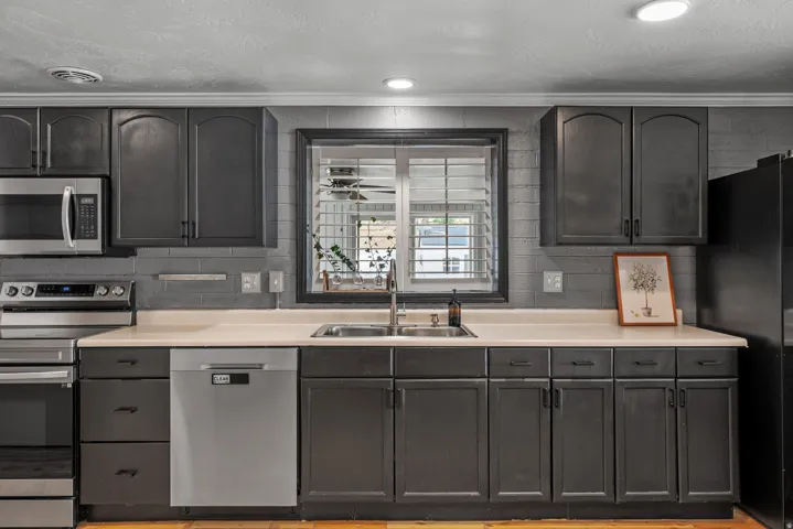 Gray cabinetry with dark hardware, undermount double-basin sink, light-toned countertops, tile backsplash, and stainless steel dishwasher
