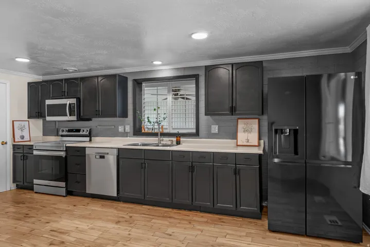 Kitchen featuring dark cabinetry, stainless steel appliances, a tile backsplash, light-toned countertops, and wood-finish flooring