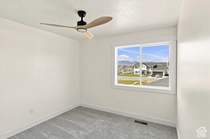 White walls, grey carpet flooring, and a modern ceiling fan with light fixture