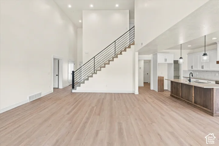 Open-concept living space featuring wood-finish flooring, a two-story ceiling, a staircase with a horizontal metal railing, and recessed lighting