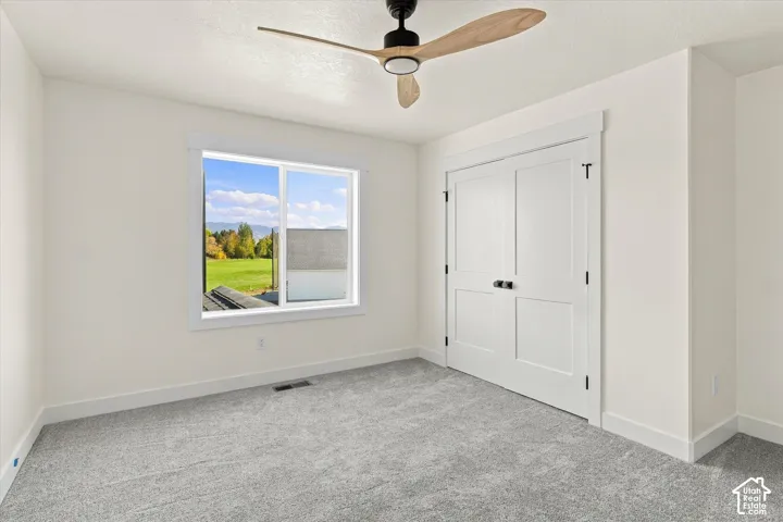 Window with white trim, light-colored carpet, white walls, white paneled doors, and a ceiling fan with wood-finish blades