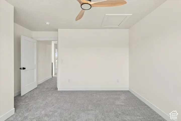 Light gray carpeted flooring, a ceiling fan with wood-finish blades, and a white interior door with black hardware