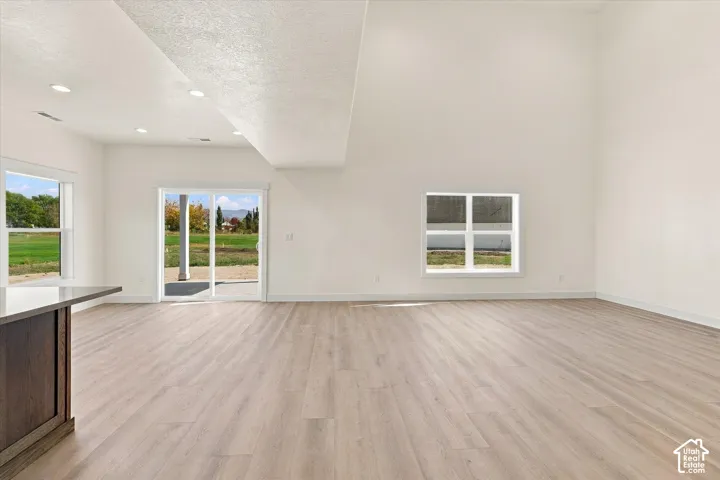 High vaulted ceilings, recessed lighting, wood-finish flooring, sliding glass patio door, and multiple windows providing ambient light