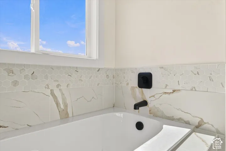 Built-in soaking tub with a matte black faucet, hexagonal mosaic tile detailing, and a large window