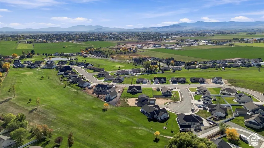 Aerial perspective of a residential development with established homes and new construction, featuring golf course access, paved streets, and a mountainous backdrop