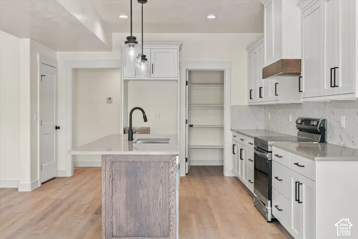 Kitchen featuring a wood-finish island with integrated sink, white cabinetry with matte black hardware, stainless steel range, and wood-finish flooring