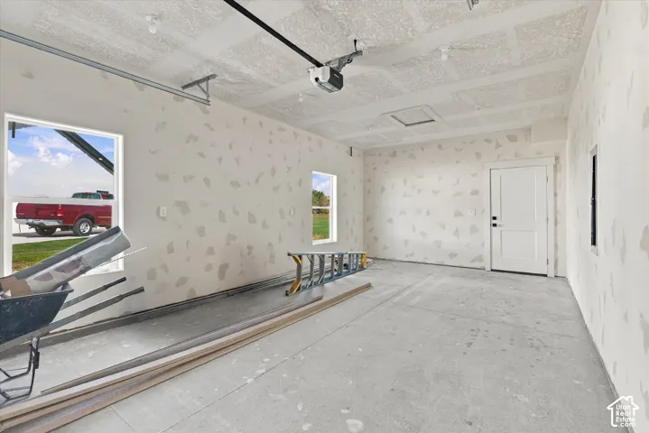 Concrete flooring, white interior door with black hardware, window openings, overhead lighting, and an automatic garage door opener mechanism