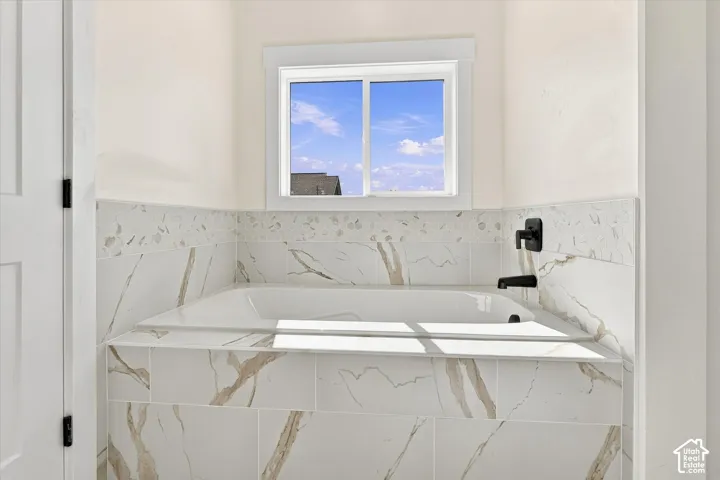Built-in soaking tub with a tiled surround, accent mosaic tiling, and a matte black faucet