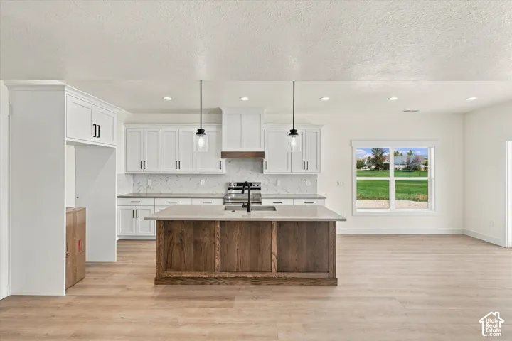 Spacious kitchen featuring white cabinetry, a wood-finish island, light-toned countertops, and wood-finish flooring