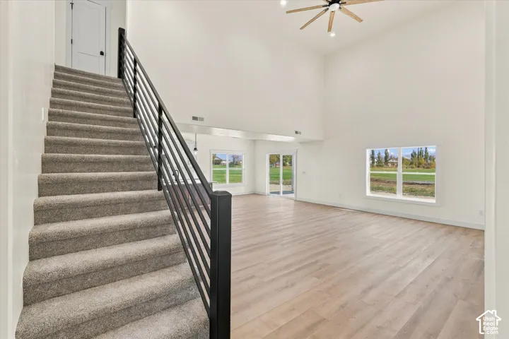 Vaulted ceilings with a wood-finish ceiling fan, wood-finish flooring, and multiple large windows