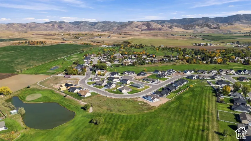 Residential development featuring cul-de-sac streets, manicured green spaces, a pond, and distant mountain backdrops