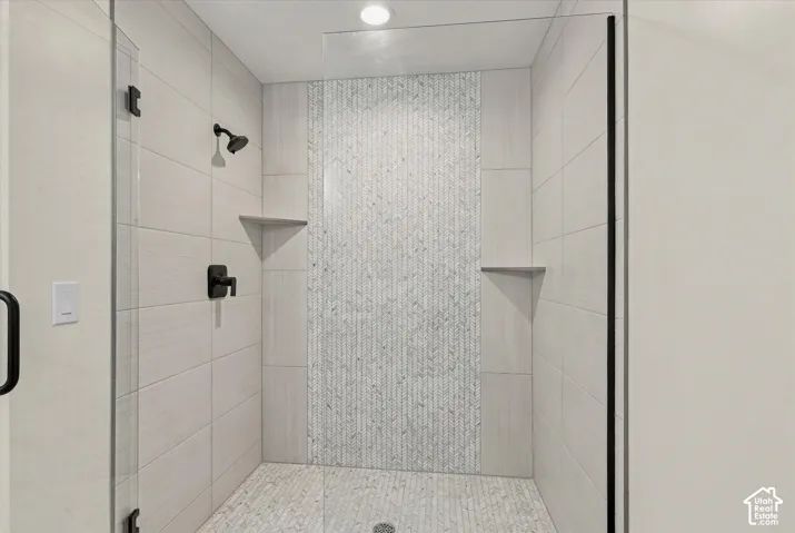 Shower enclosure with clear glass paneling, matte black fixtures, integrated corner shelving, and a decorative tiled accent wall