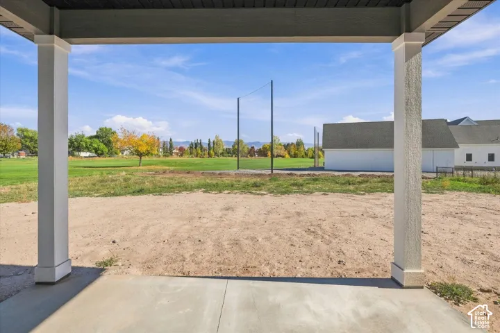 Covered concrete patio with white columns and a dark soffit, overlooking an expansive dirt yard