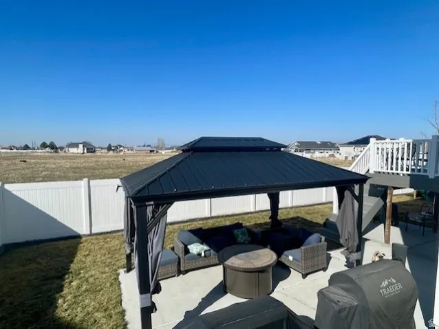 Expansive concrete patio with a permanent gazebo, a privacy fence, and a multi-level deck featuring white railings