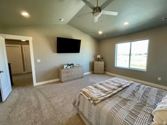 Primary bedroom; Vaulted ceiling with a ceiling fan, recessed lighting, carpeted flooring, and a large window