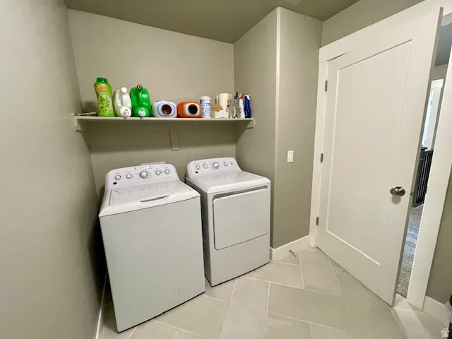 Utility room featuring light grey wall paint, a white wall-mounted shelf, light-colored tile flooring, and a white interior door with brass hardware