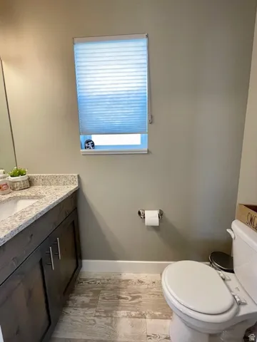 Main level half bath.  Wood-finish flooring, dark wood-finish vanity with silver-tone hardware, light-toned countertop, and window with light-filtering blinds.