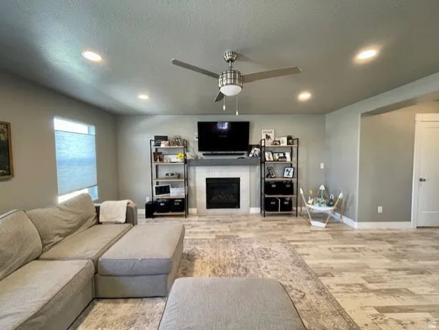 Living area featuring a fireplace with a tiled surround and mantel, wood-finish flooring, recessed lighting, and a ceiling fan.