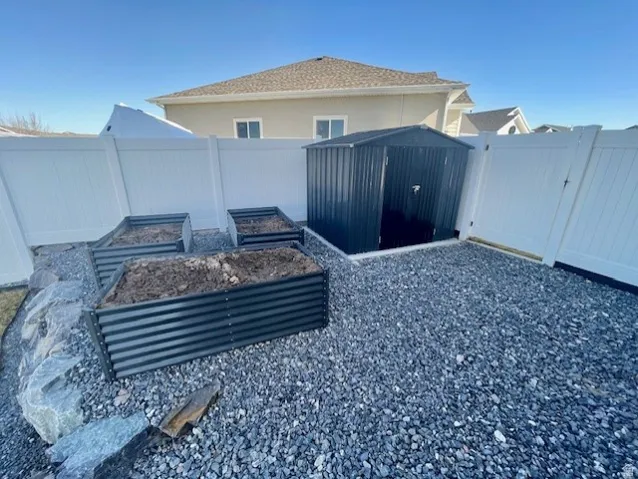 White privacy fencing, raised garden beds, a storage shed, and a gravel ground cover