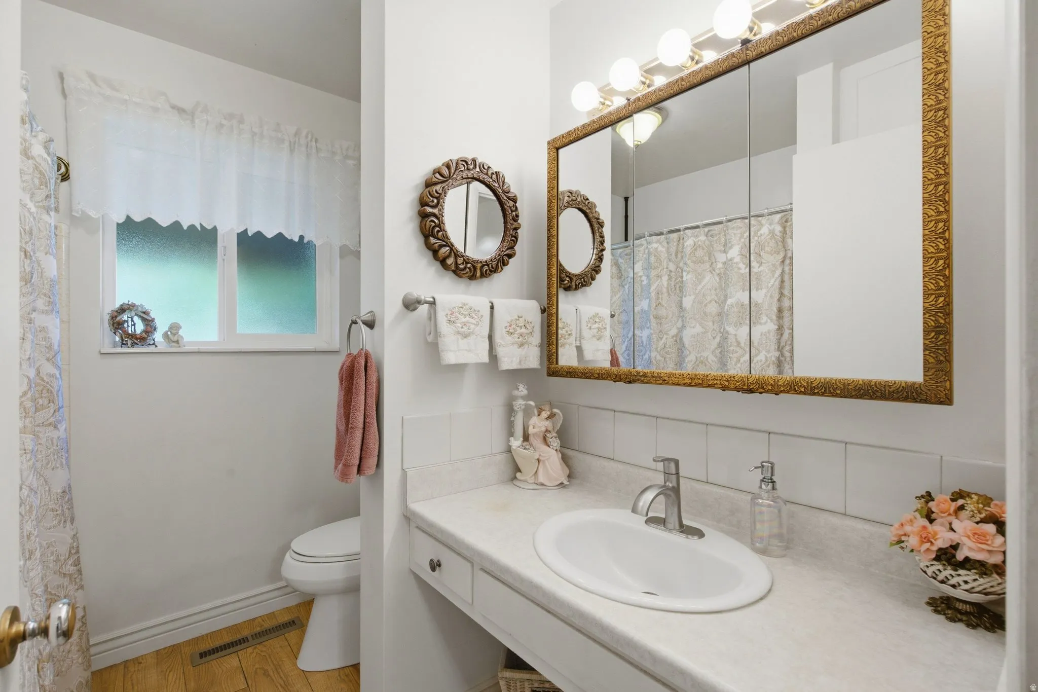 Vanity with an integrated sink, decorative framed medicine cabinet with overhead lighting, wood-finish flooring, and a privacy window