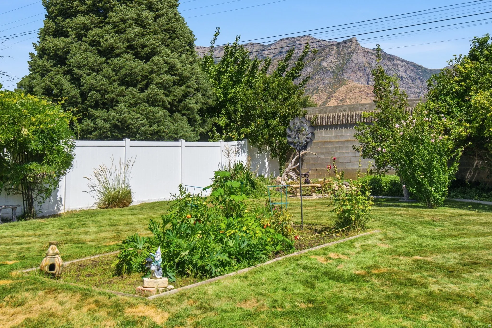 Expansive backyard featuring a manicured lawn, established garden beds, a white privacy fence, and a distant mountain backdrop