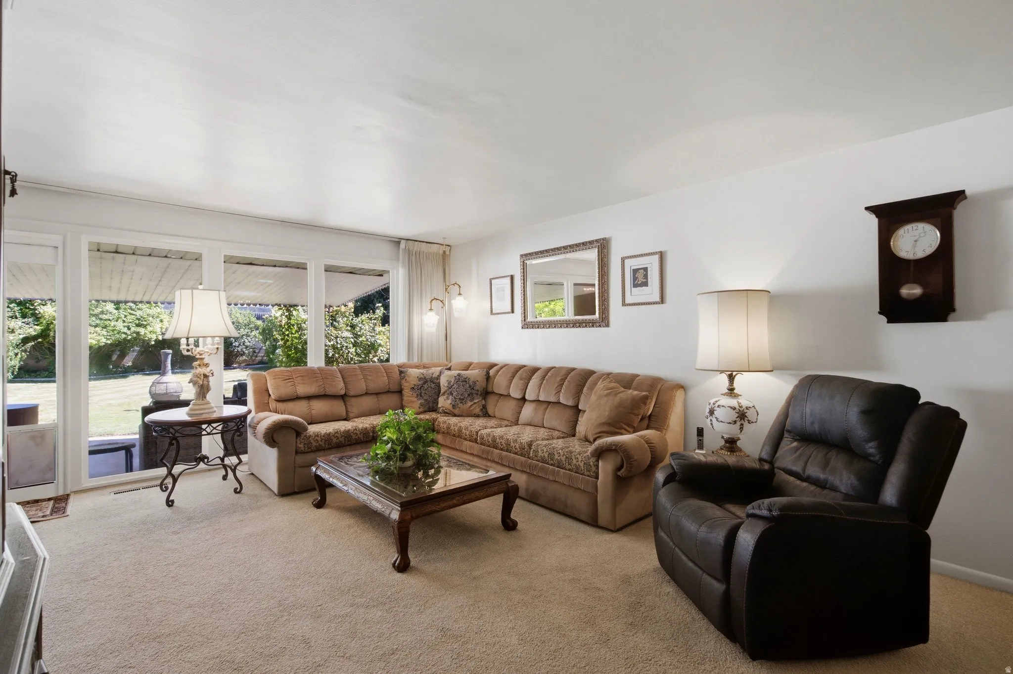 Carpeted flooring, white walls, and a large window overlooking a landscaped outdoor area