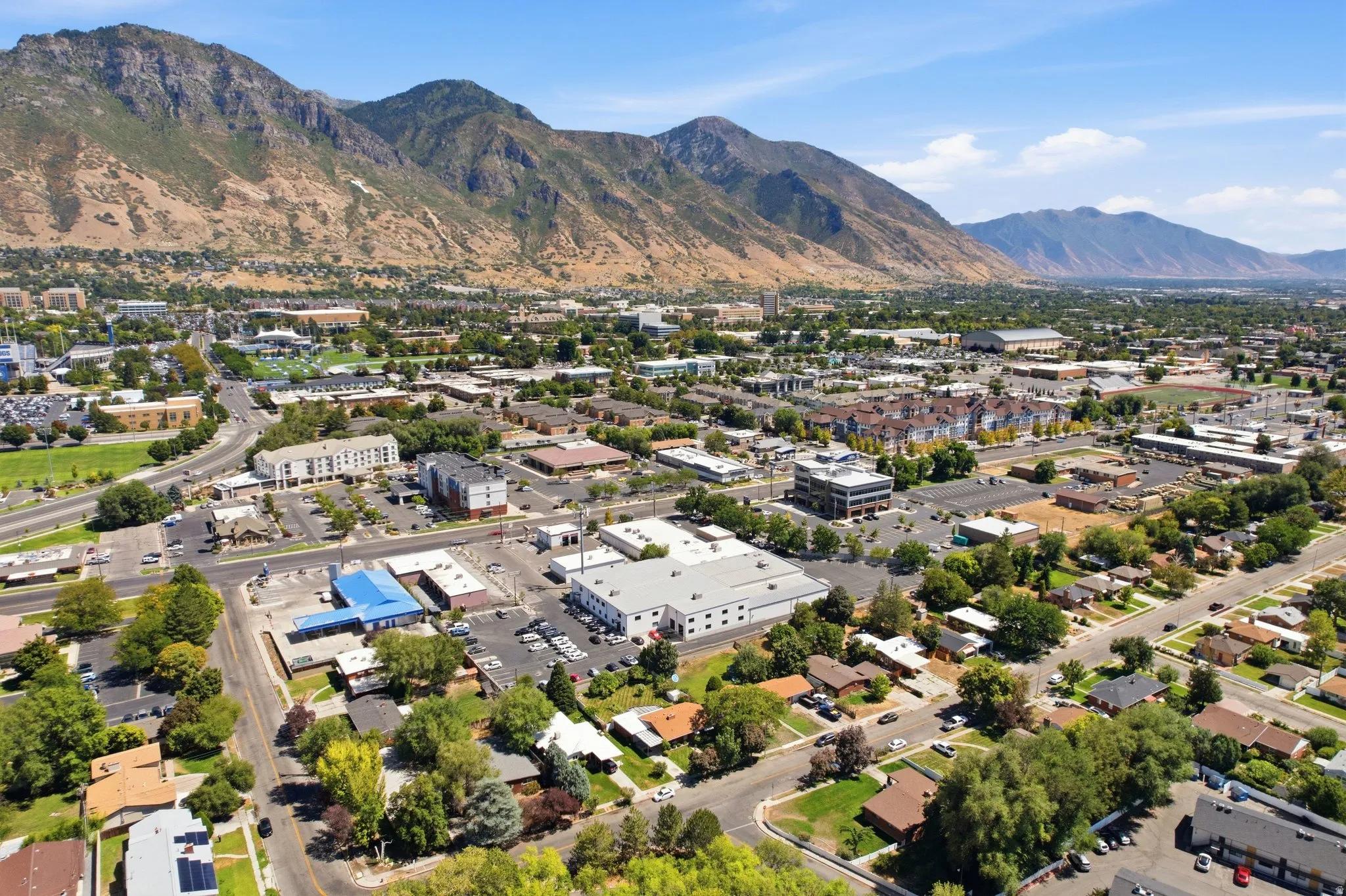 Expansive urban setting with a mountain backdrop, featuring a network of roads, commercial buildings, residential structures, and established trees