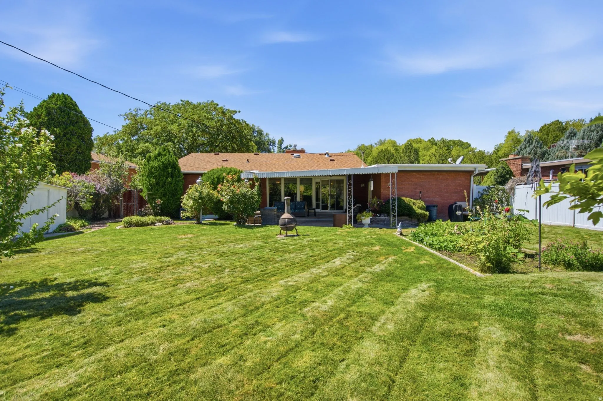 Expansive green lawn with mature landscaping, covered patio, and garden area