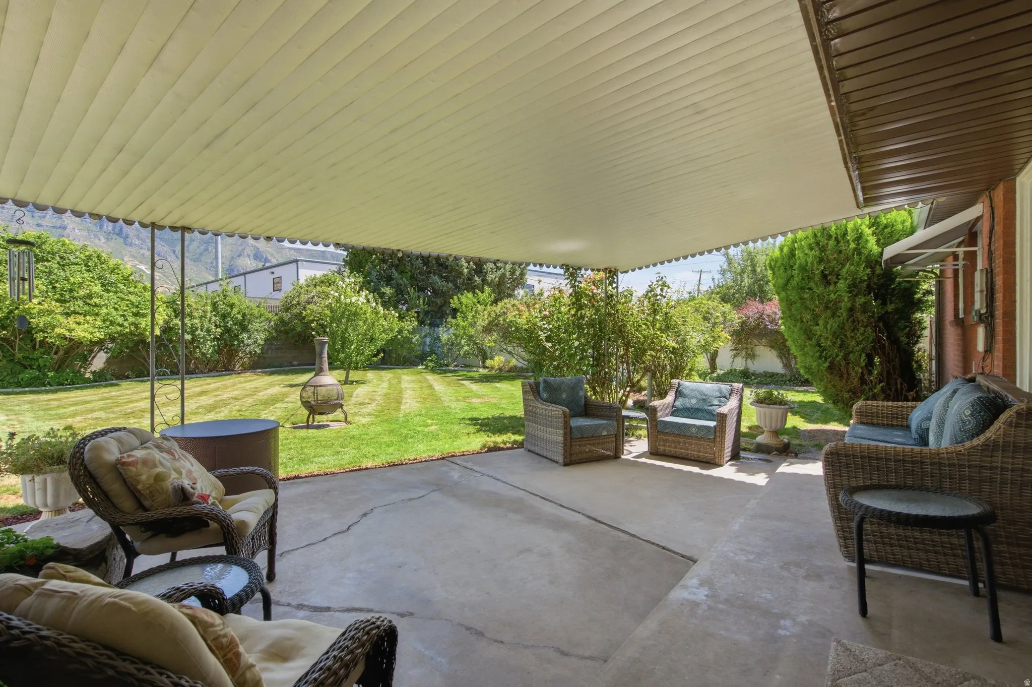 Expansive concrete patio with a full-length overhead cover, offering direct access to a large, landscaped yard featuring mature trees and green lawn