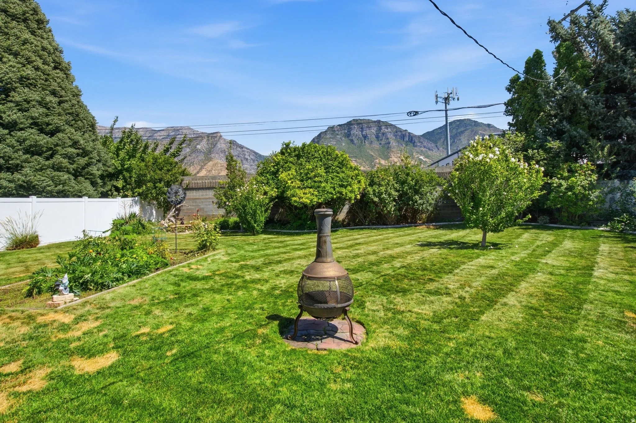 Expansive grassy area with a privacy fence, mature trees, and mountainous terrain in the background