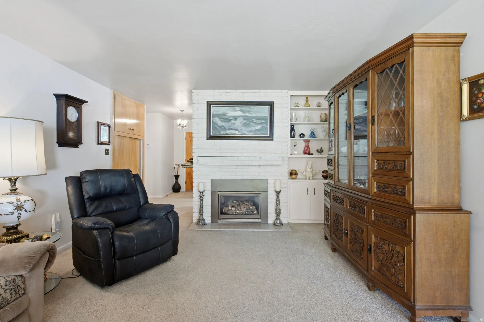 Carpeted living area featuring a white brick fireplace, built-in shelving, and light wood cabinetry