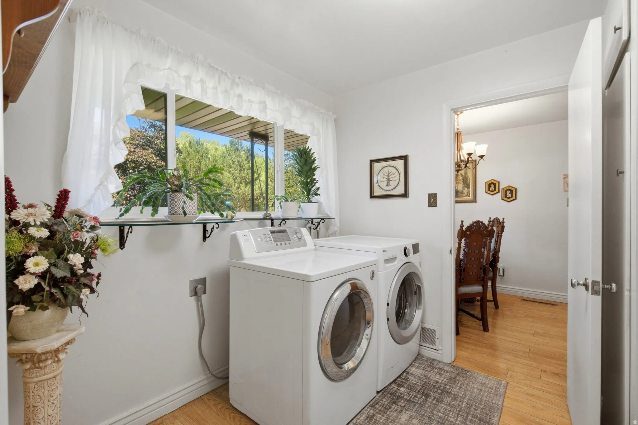 Laundry area featuring a large window, wood-finish flooring, and a doorway to an adjacent room with a chandelier