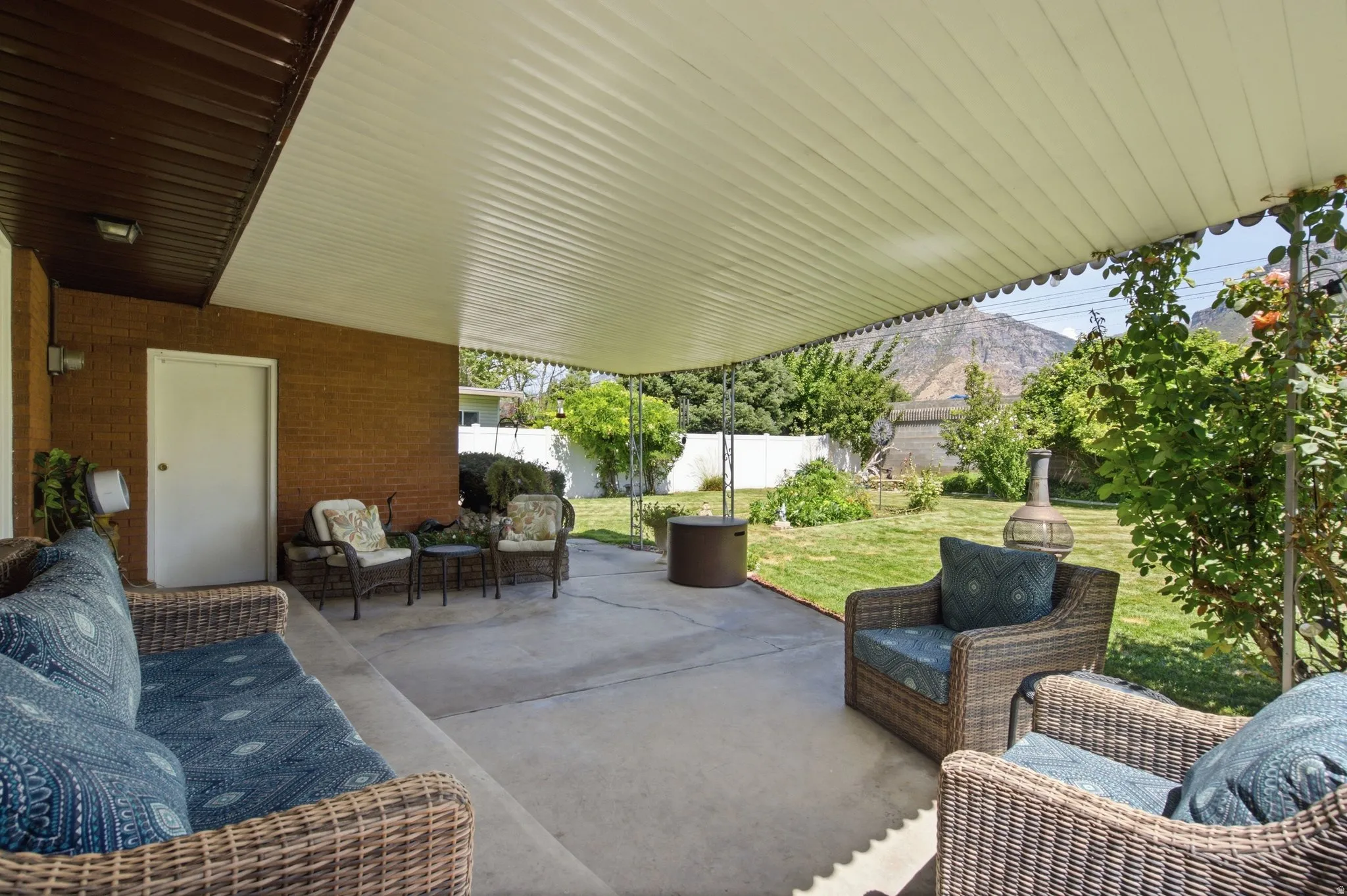 Covered concrete patio, brick exterior, expansive grassy yard, mature landscaping, mountain backdrop