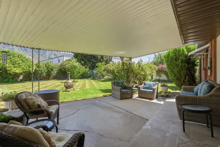 Expansive concrete patio with a full-length overhead cover, offering direct access to a large, landscaped yard featuring mature trees and green lawn