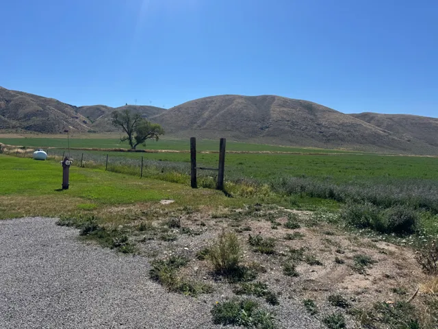 Expansive green field with natural landscaping, bordered by a gravel area and distant hills