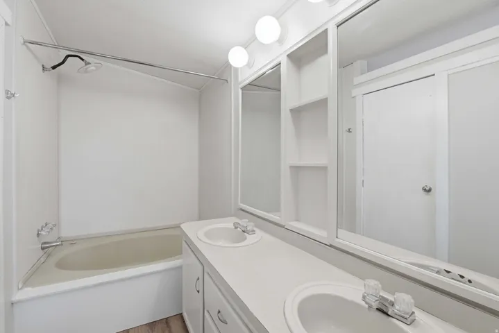 Double vanity with integrated sinks, built-in storage shelving, and a combination shower and bathtub