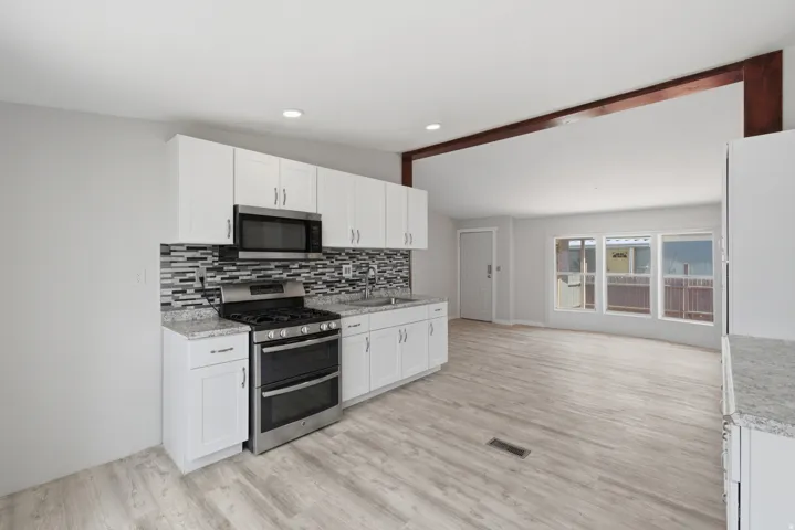 Kitchen featuring white cabinetry, granite-style countertops, mosaic tile backsplash, and stainless steel appliances