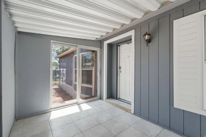 Enclosed patio with tile flooring, white entry door, and sliding glass doors