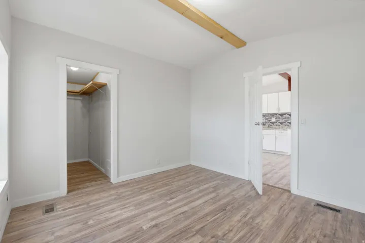 Neutral-toned walls, wood-finish flooring, exposed ceiling beam, built-in closet shelving, and a white interior door