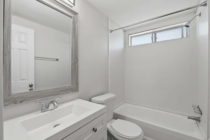 Integrated shower/tub combination, vanity with single basin sink, framed mirror, wall-mounted light fixture, and horizontal window