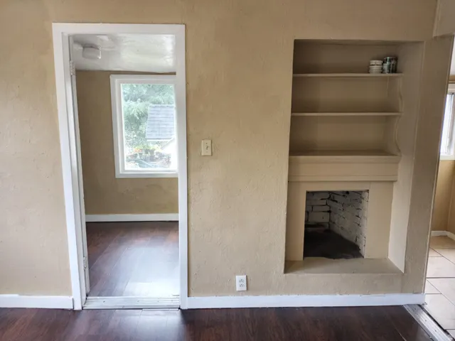 Built-in shelving, decorative fireplace, wood-finish flooring, white window trim