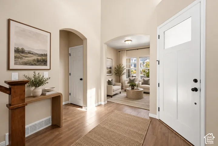 Virtually Staged. Entryway featuring high ceilings, wood-finish flooring, white paneled entry door with an upper glass insert, and arched architectural openings